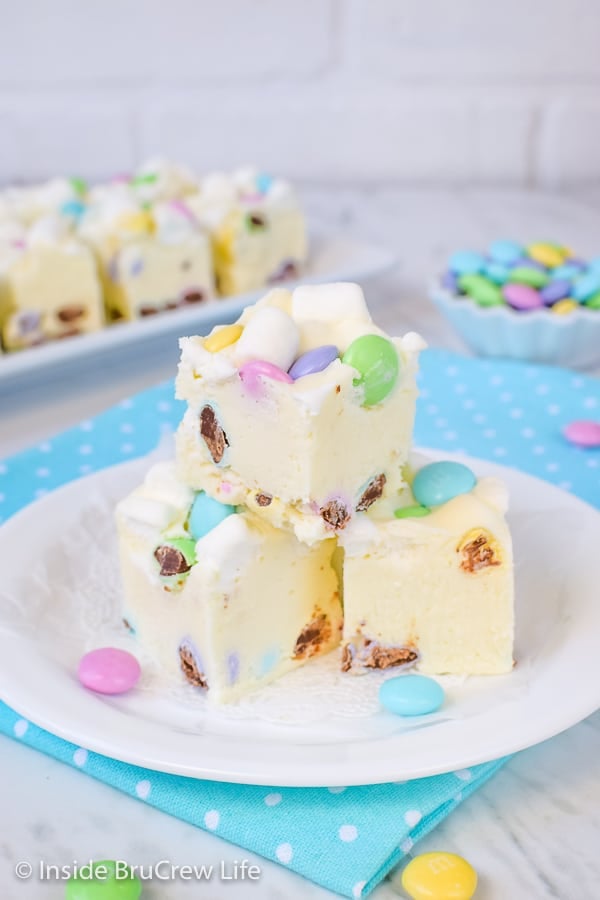 3 pieces of white fudge loaded with marshmallows and chocolate candies on a white plate on top of a blue polka dot napkin.