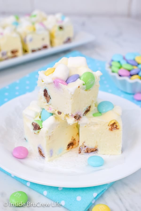 3 pieces of white fudge loaded with marshmallows and chocolate candies on a white plate on top of a blue polka dot napkin.