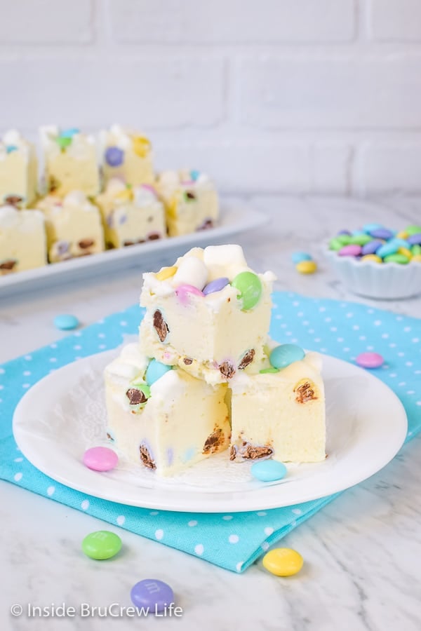 3 pieces of white fudge loaded with marshmallows and chocolate candies on a white plate on top of a blue polka dot napkin.