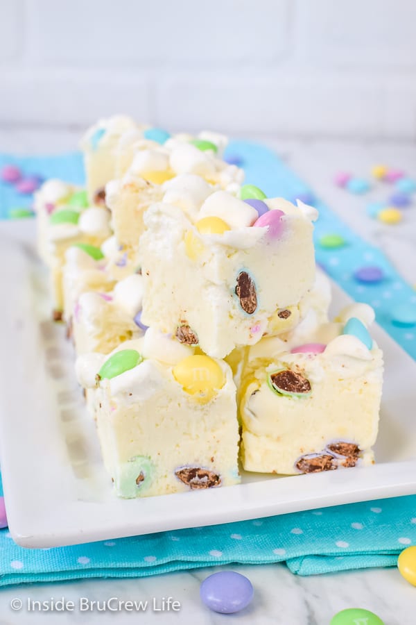 Multiple pieces of white fudge loaded with marshmallows and chocolate candies on a white plate on top of a blue polka dot napkin.