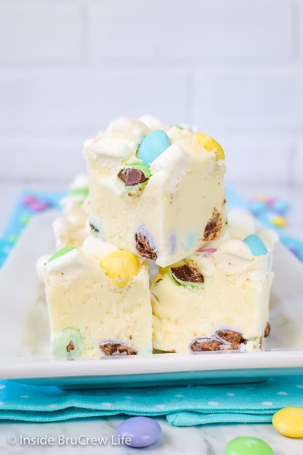 3 pieces of white fudge loaded with marshmallows and chocolate candies on a white plate on top of a blue polka dot napkin.