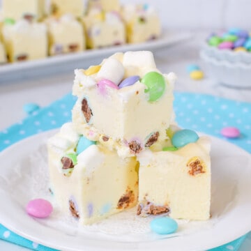 3 pieces of white fudge loaded with marshmallows and chocolate candies on a white plate on top of a blue polka dot napkin.