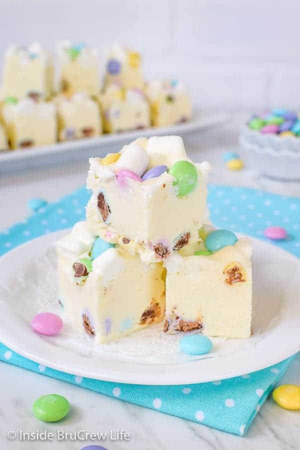 3 pieces of white fudge loaded with marshmallows and chocolate candies on a white plate on top of a blue polka dot napkin.