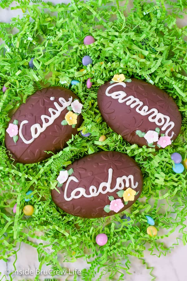Green Easter grass with three large peanut butter eggs decorated with chocolate names and candy flowers in it.