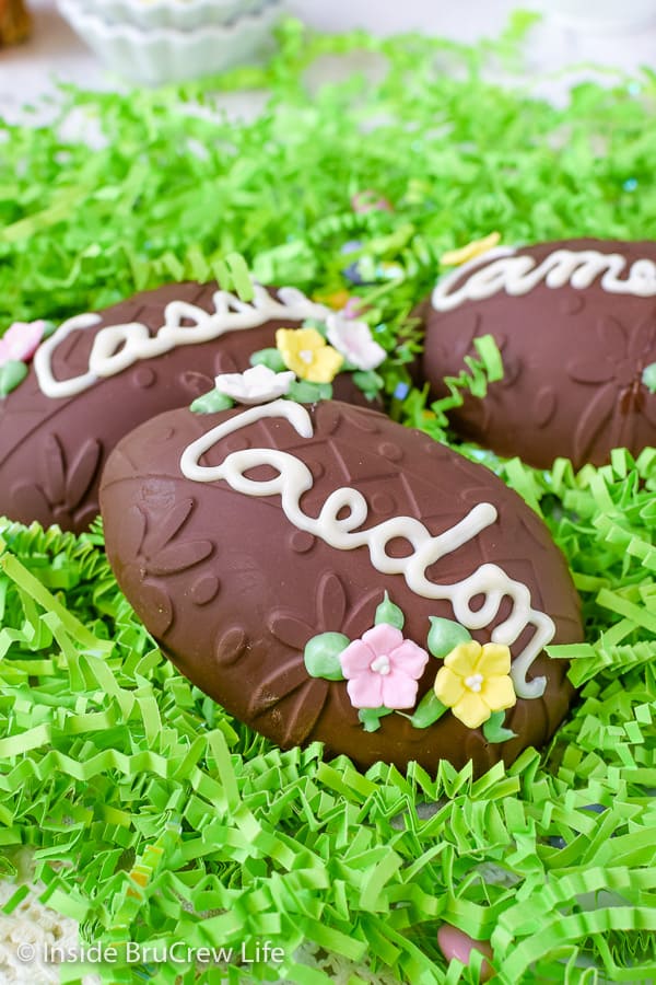 A close up picture of a Reese's egg decorated with a name and flower candies in green Easter grass.