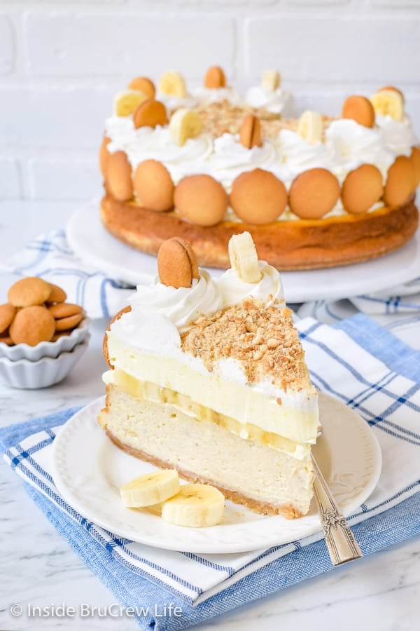 A slice of banana pudding cheesecake on a white plate with more cheesecake behind it.