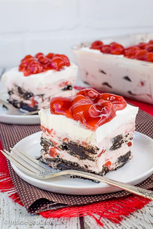 Two white plates with squares of cherry oreo icebox cake on them with cherry pie filling on top
