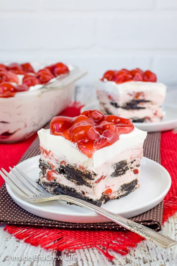 Two white plates on a brown towel with cherry oreo icebox squares on them with cherry pie filling on top