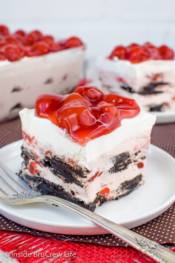 Two white plates on a brown towel with squares of cherry oreo icebox cake on them and cherry pie filling on top