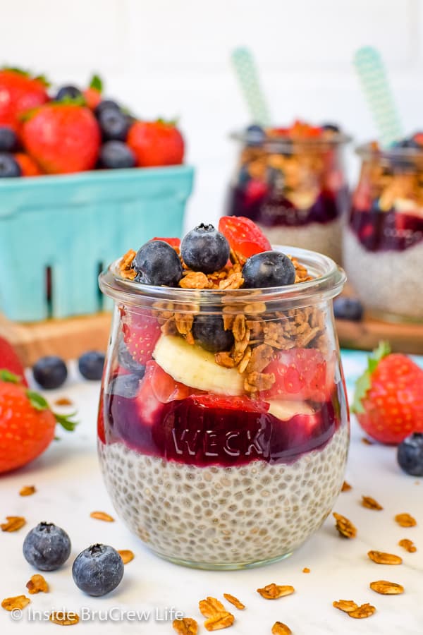 A clear jar filled with layers of chia pudding, blackberry preserves, fruit, and granola.