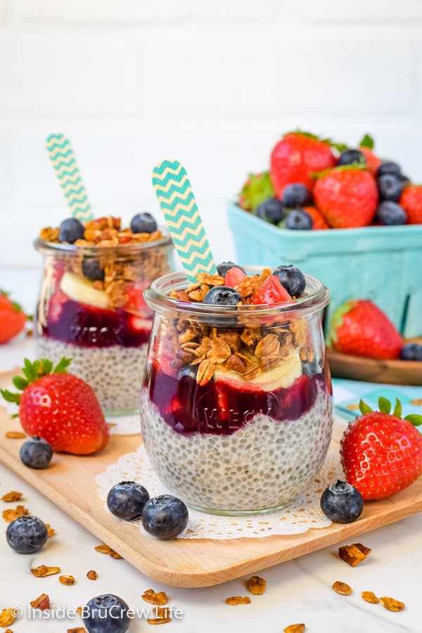 Two clear jars on a wood tray filled with chia pudding, fruit, and granola.