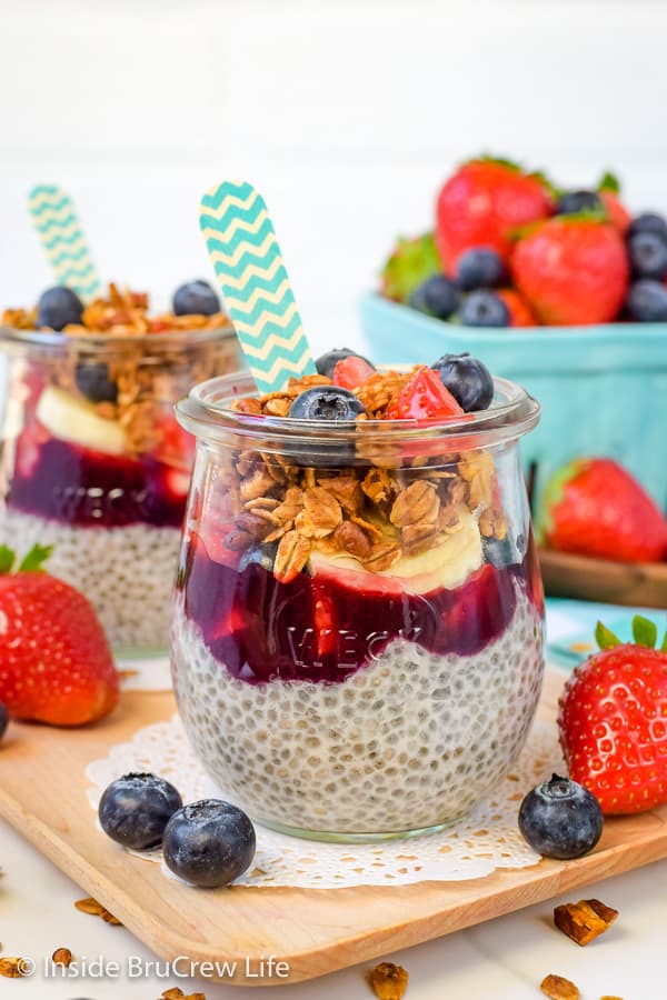 Two clear jars on a wooden tray filled with chia pudding, fruit, and granola.