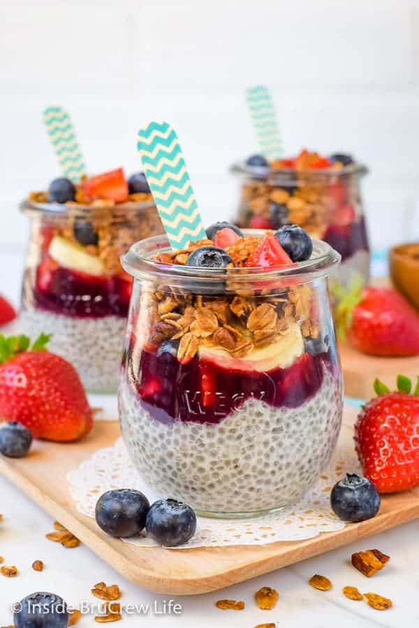 Three clear jars filled with layers of chia pudding, blackberry preserves, fruit, and granola.