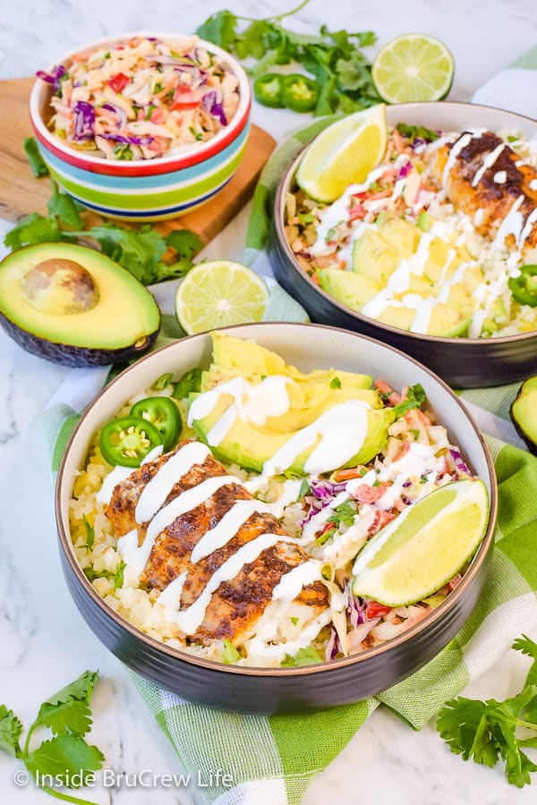 Two fish taco bowls filled with cauliflower rice, coleslaw, and baked cod.