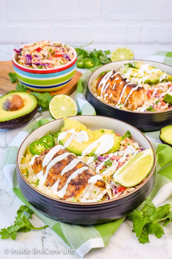 A fish taco bowl filled with baked cod, rice, coleslaw, avocado, and a lime crema.