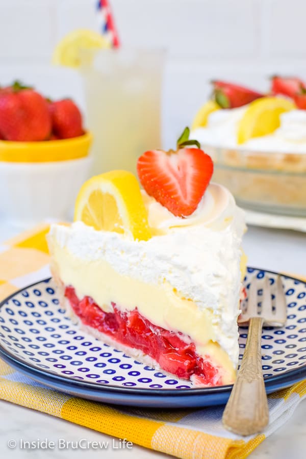 A white and blue plate with a piece of lemon cream strawberry pie on it and a pie plate behind it.