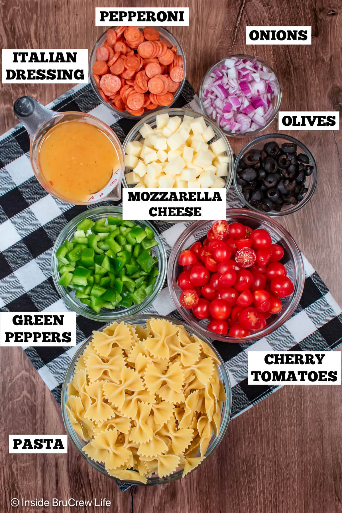 Bowls of ingredients needed to make a cold pasta salad with pizza toppings.