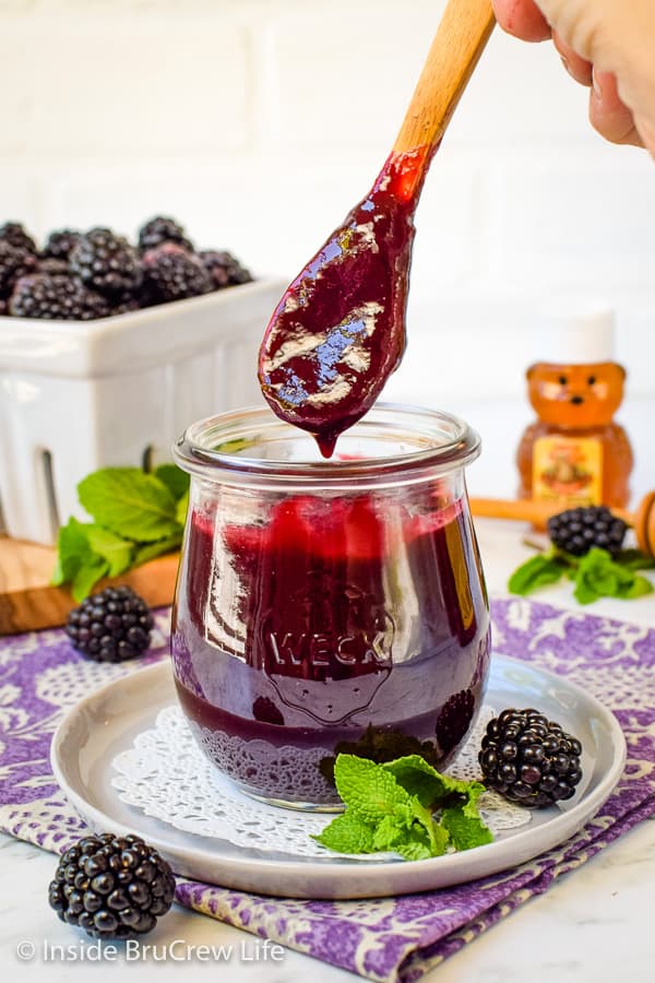 A jar of homemade blackberry preserves with a spoon lifting some out.