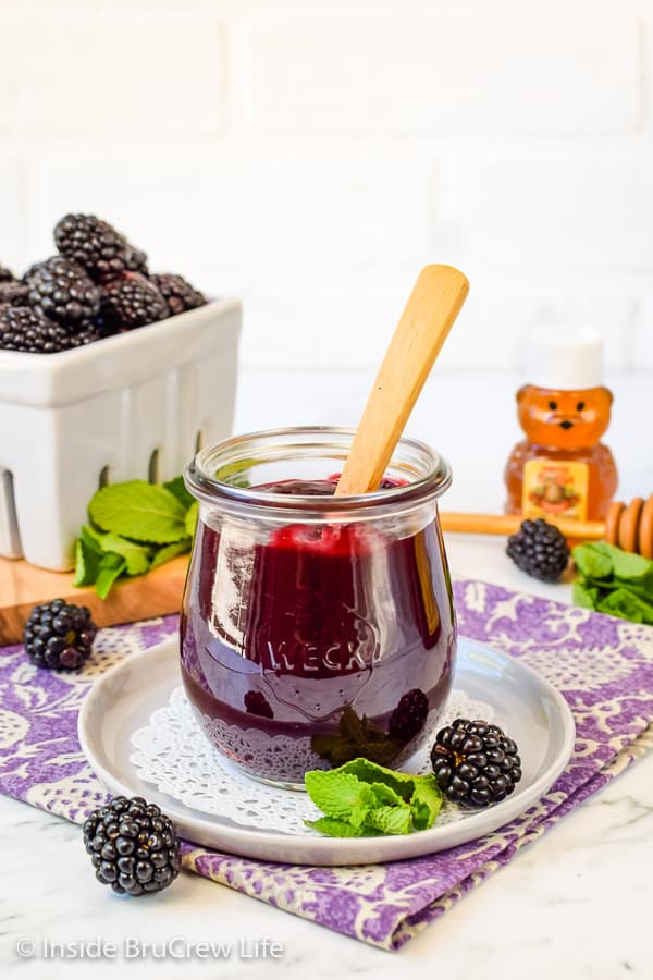A clear jar filled with blackberry preserves with a spoon in it.