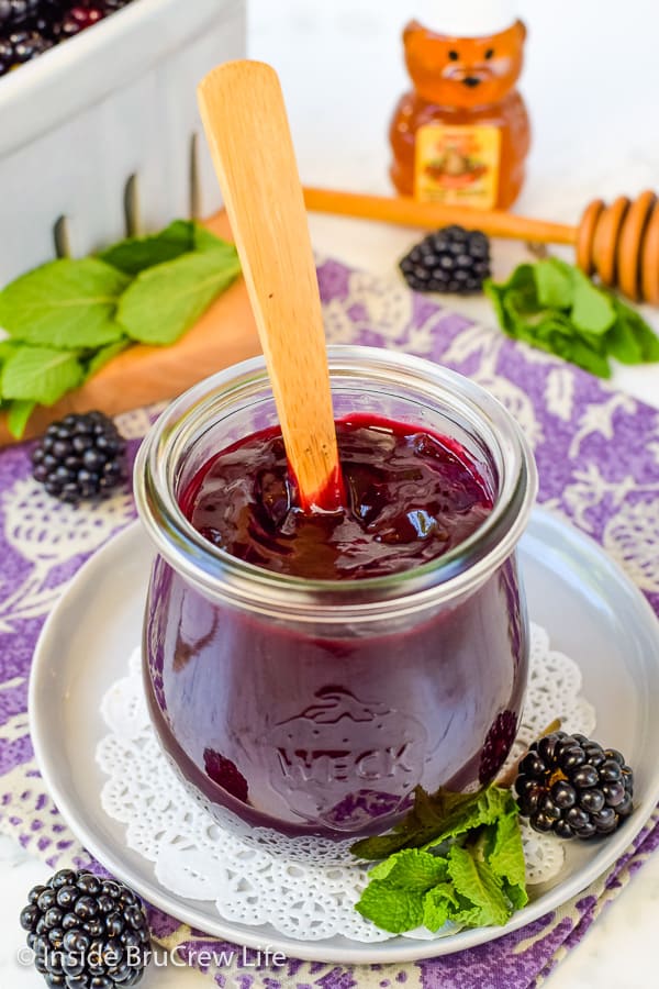 A white plate with a jar of seedless blackberry preserves on it.