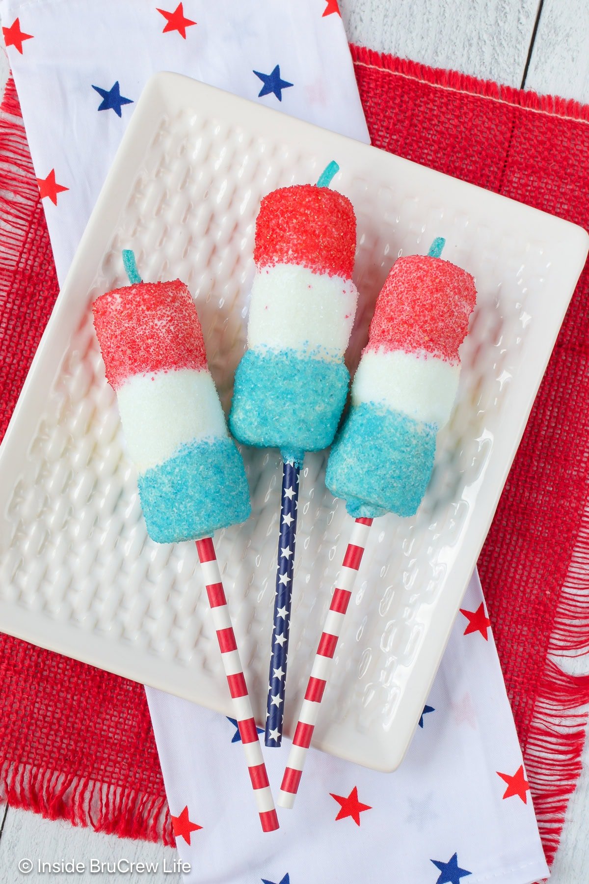 Three red white and blue marshmallow pops lying on a white plate.