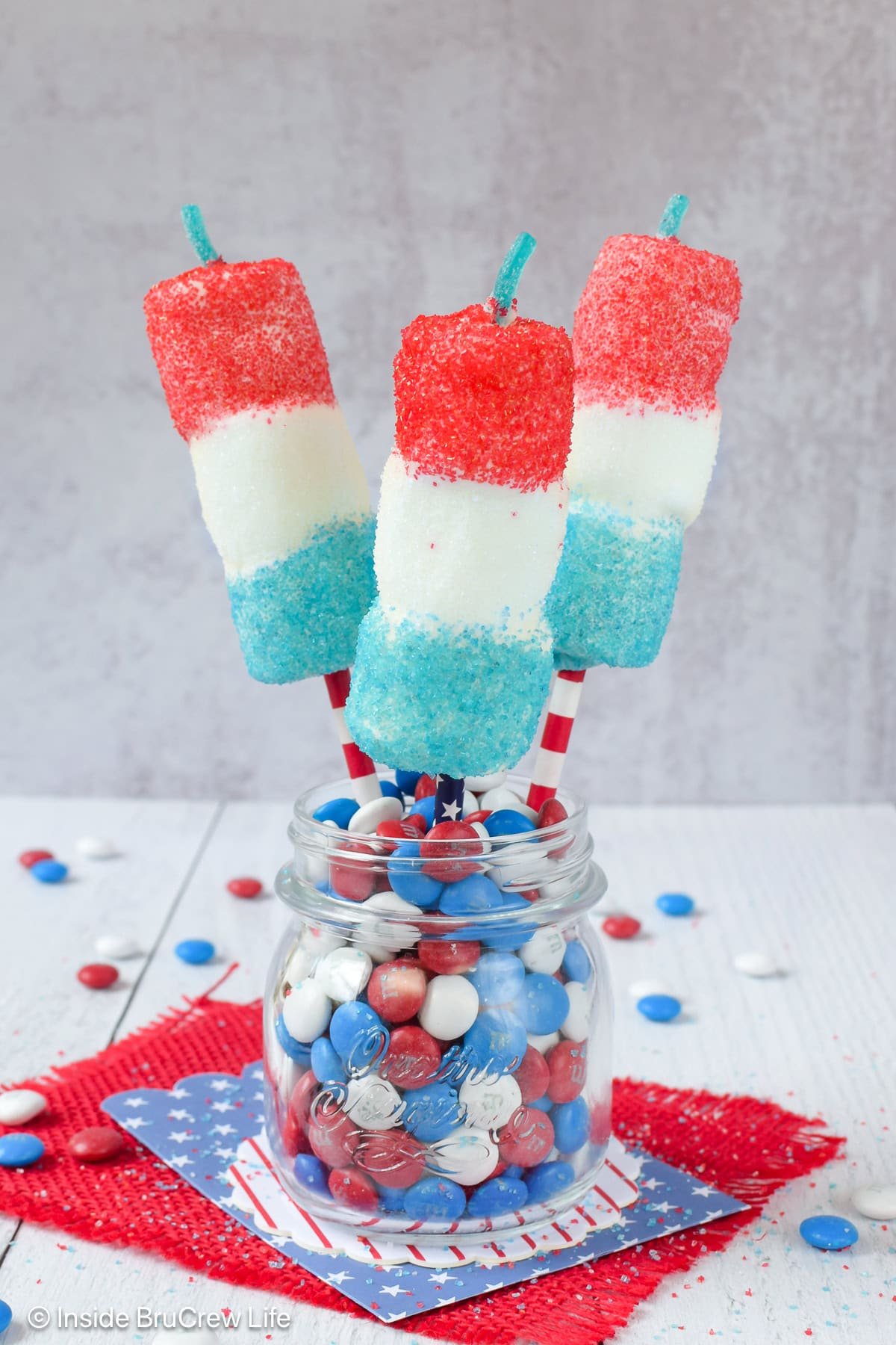 A jar of chocolate candies with three 4th of July marshmallow pops stuck in it.