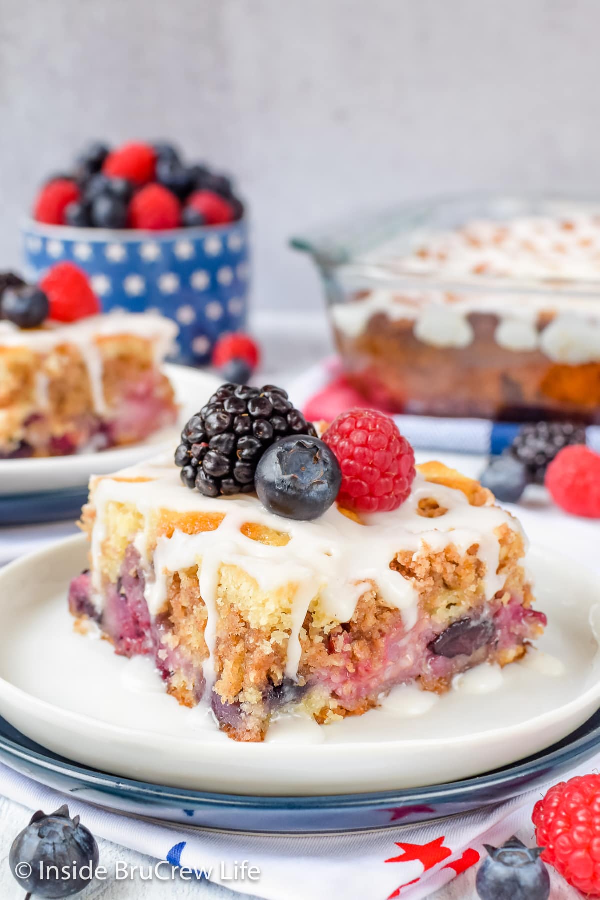 A slice of mixed berry cake on a plate with berries on top.