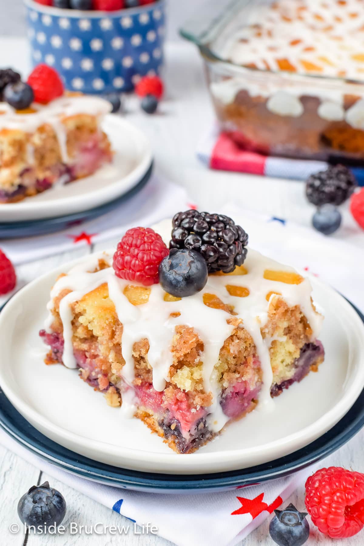 A white plate with a square of glazed berry coffee cake on it.