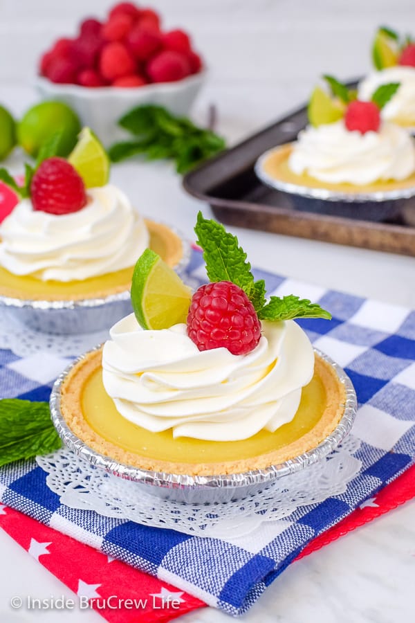 Two mini pies filled with key lime curd and topped with whipped cream and raspberries.