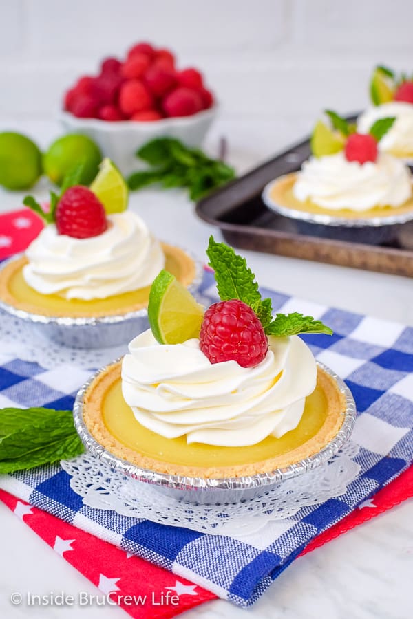 Two mini lime pies topped with Cool Whip and raspberries on a blue and white towel.