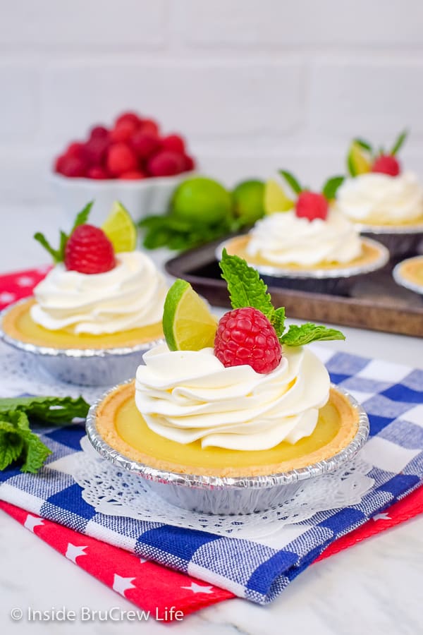 Two mini graham cracker pies filled with lime curd and topped with whipped cream and raspberries.