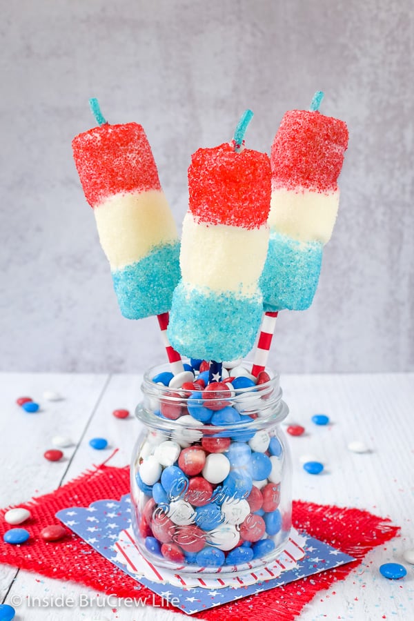 Three firecracker marshmallow pops stuck in a jar of red white and blue m&m candies.