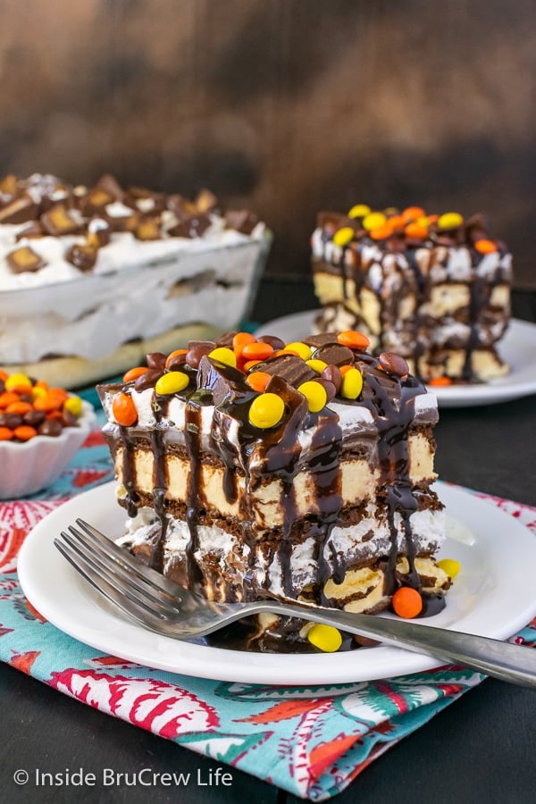 Two white plates with squares of ice cream sandwich cake topped with hot fudge and Reese's candies.