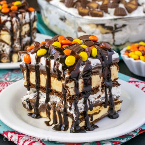 A white plate with a slice of ice cream sandwich cake topped with Reese's candies and chocolate.