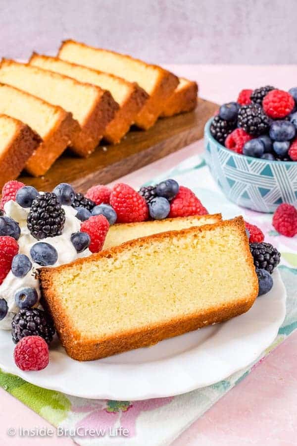 A white plate with a slice of  pound cake, whipped cream, and berries on it.