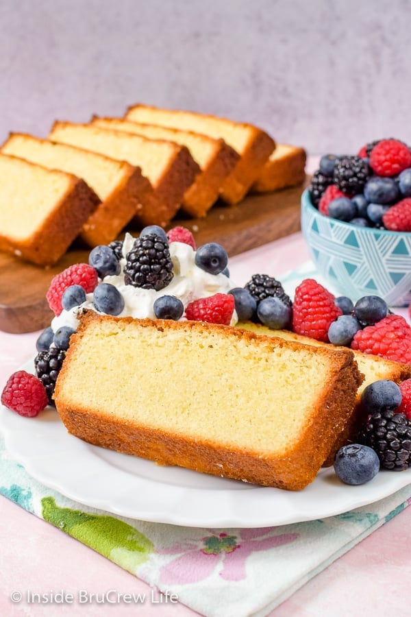 Vanilla pound cake slices and berries on a white plate with a tray of pound cake behind it.