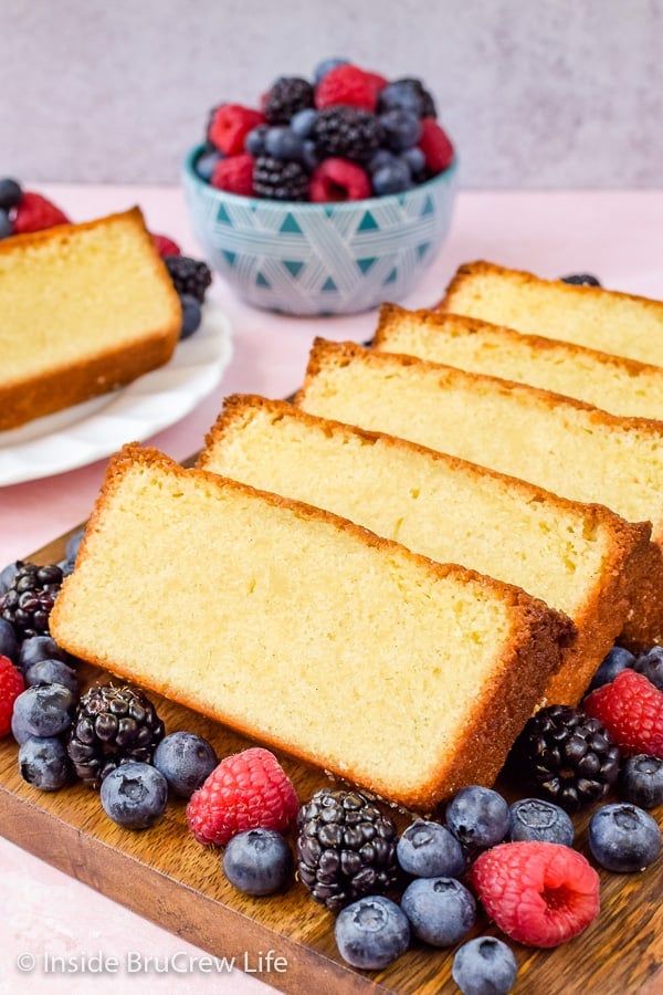 Slices of vanilla pound cake on a wooden tray surrounded by fresh berries.