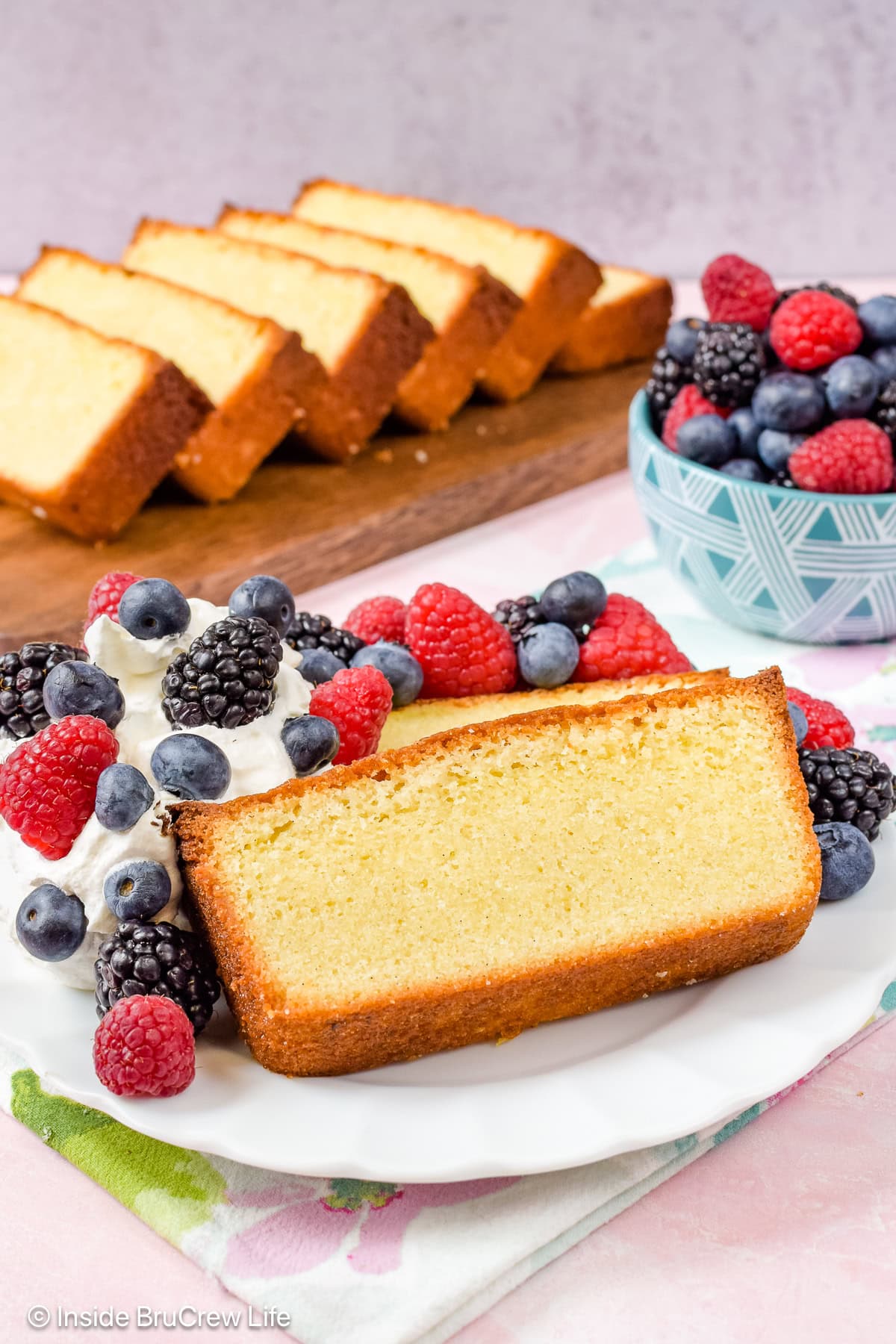 A white plate with vanilla pound cake slices, whipped cream, and berries on it.
