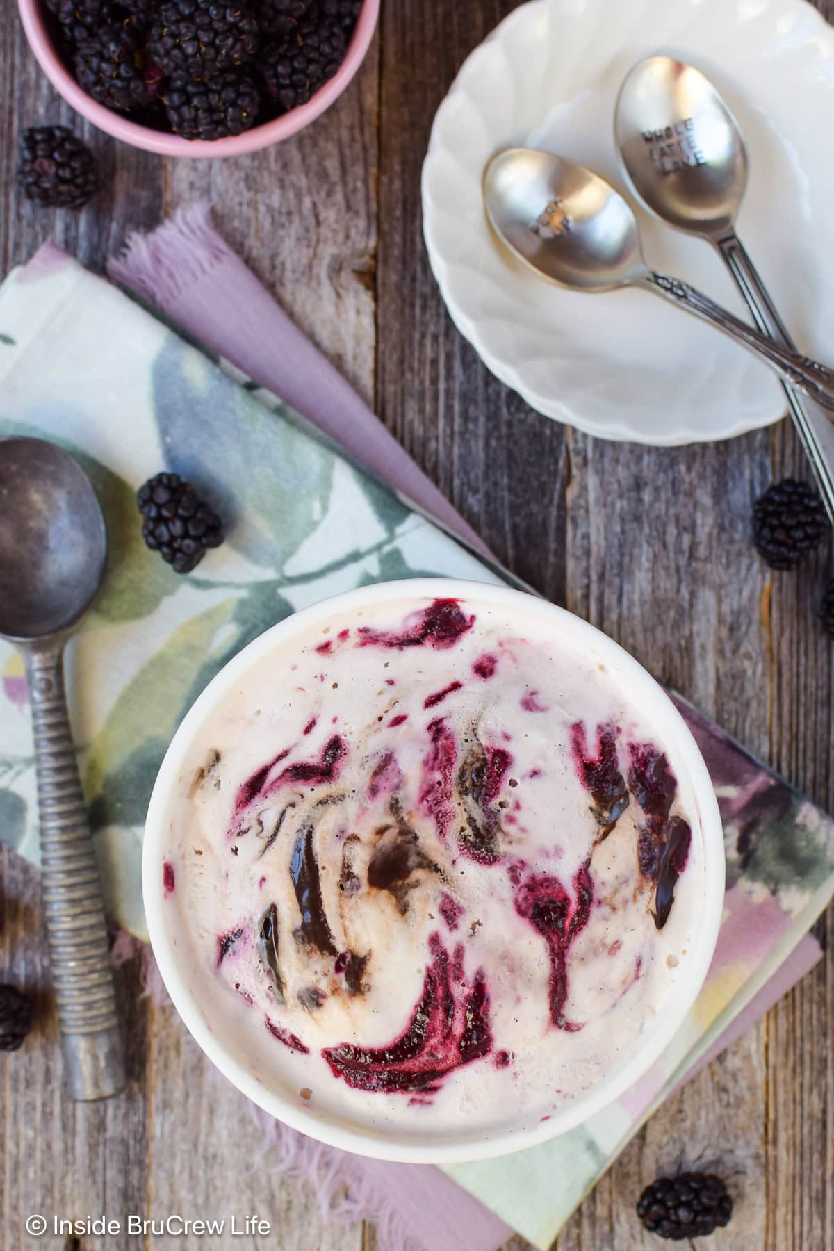 A container of ice cream with fudge and fruit swirls on top.