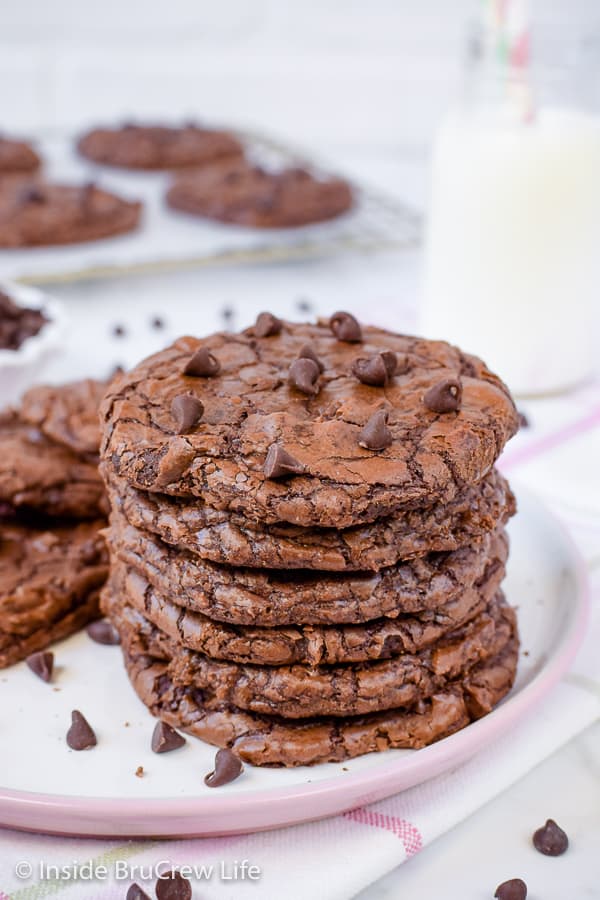 A stack of six brownie cookies on a pink and white plate with mini chocolate chips scattered around it. 