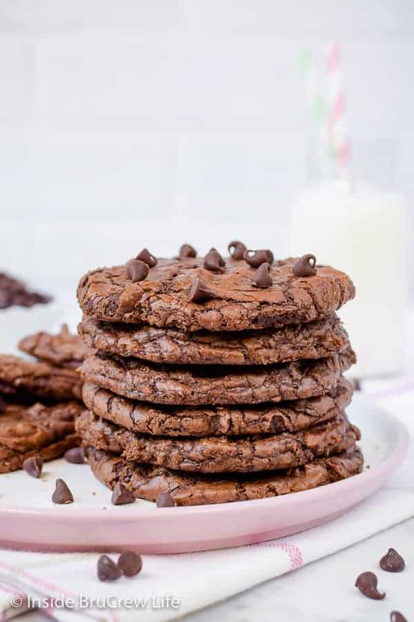 A pink plate with a stack of six brownie cookies on it and mini chocolate chips scattered around it.