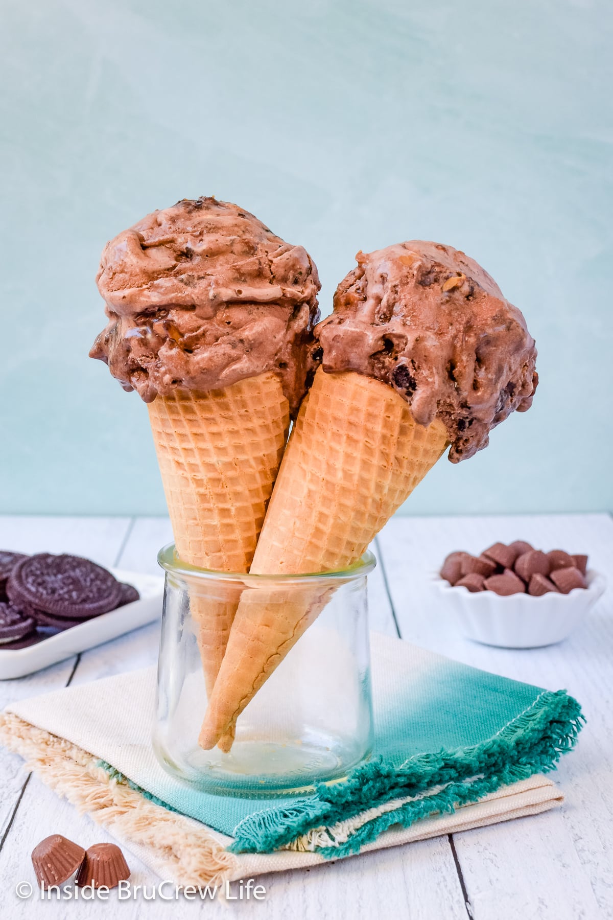 Two sugar cones with scoops of chocolate ice cream.