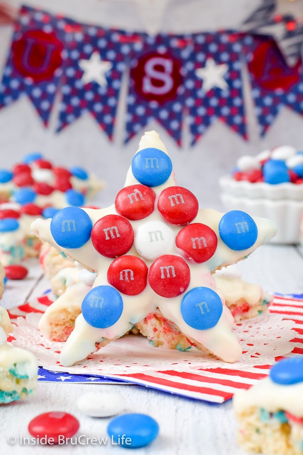 A rice krispie treat star decorated with white chocolate and red white and blue M&M candies standing up on a white board