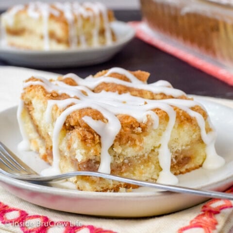 A white plate with a slice of sour cream coffee cake with a drizzle of glaze on it.