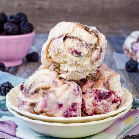 A white bowl with scoops of vanilla bean ice cream with blackberry and hot fudge swirls.