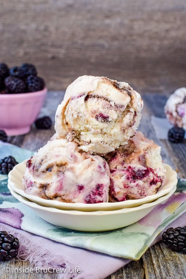 A white bowl filled with scoops of homemade vanilla ice cream with blackberry and hot fudge swirls.