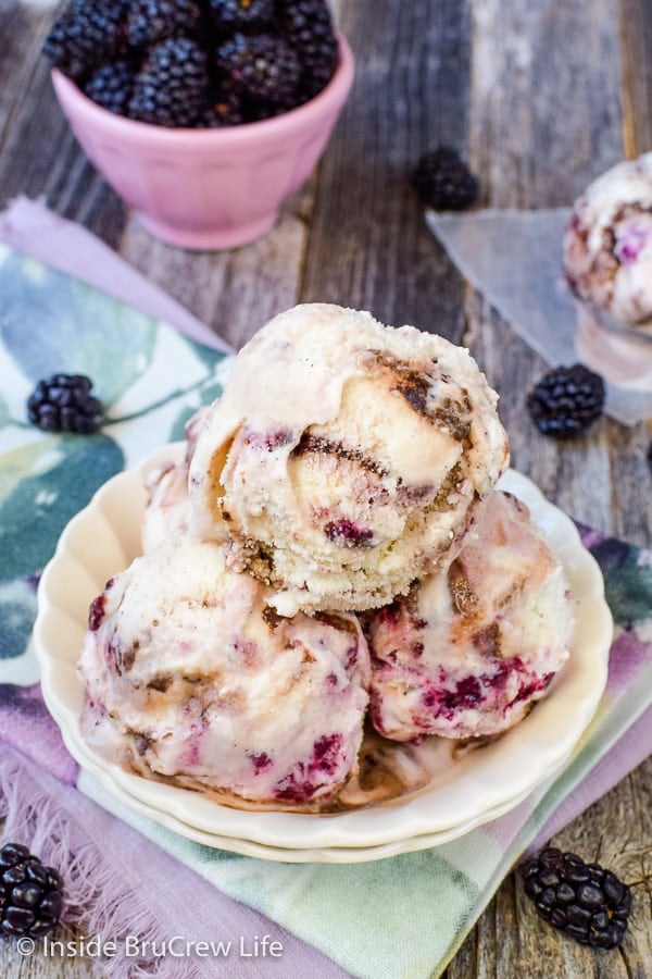 A white bowl filled with scoops of vanilla bean blackberry fudge ice cream and blackberries behind it.