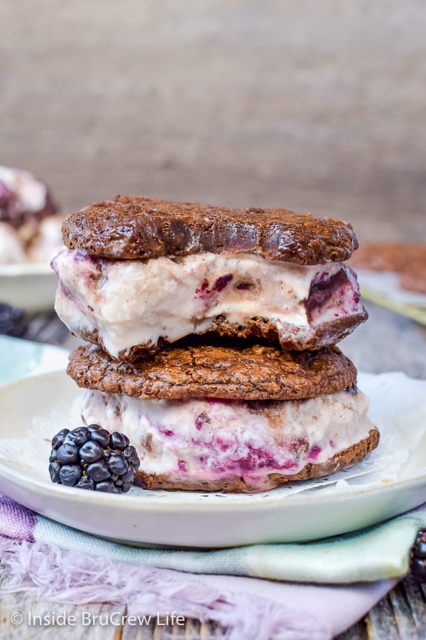 Two brownie ice cream sandwiches filled with vanilla blackberry ice cream on a white plate.