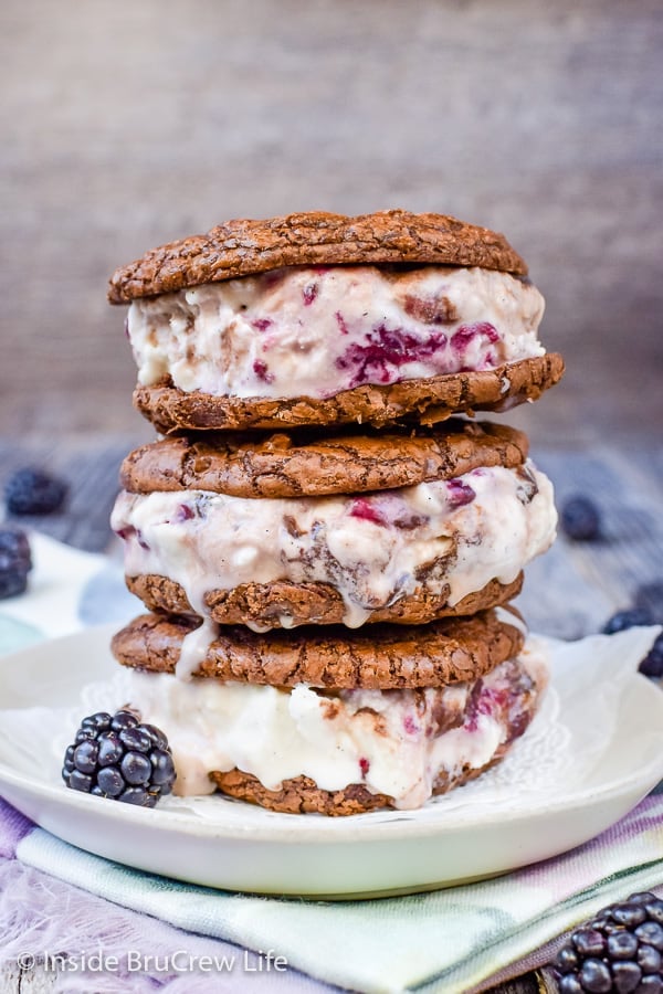 Three brownie ice cream sandwiches filled with blackberry fudge ice cream stacked on top of each other on a white plate.