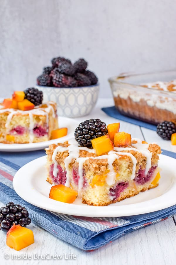 Two plates with pieces of peach blackberry coffee cake with drizzles of glaze on top.